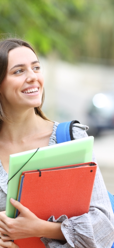 young woman smiling and walking with textbooks and folders